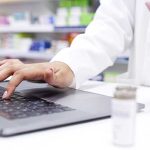 Hands of chemist in a pharmacy checking medicine on a laptop at a dispensary. Closeup of a pharmacist filling a prescription, or checking information online for medication inside a drugstore