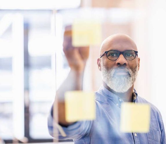 Portrait of businessman taking adhesive note from glass wall in office