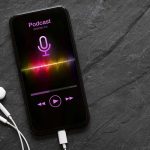 Earphones and mobile phone with podcast app on screen on black background